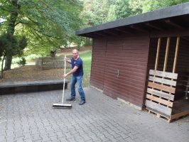 Vorstand Dieter Waller fegt vor dem Eingang der Hütte die Blätter weg  ...